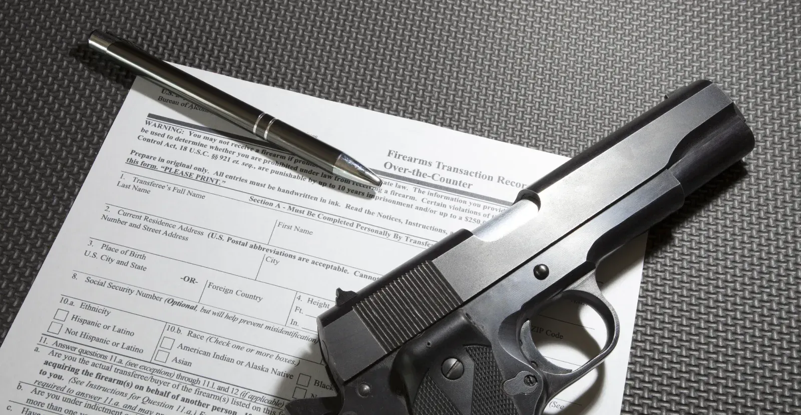 A handgun laying on a Firearms Transaction Record and pen