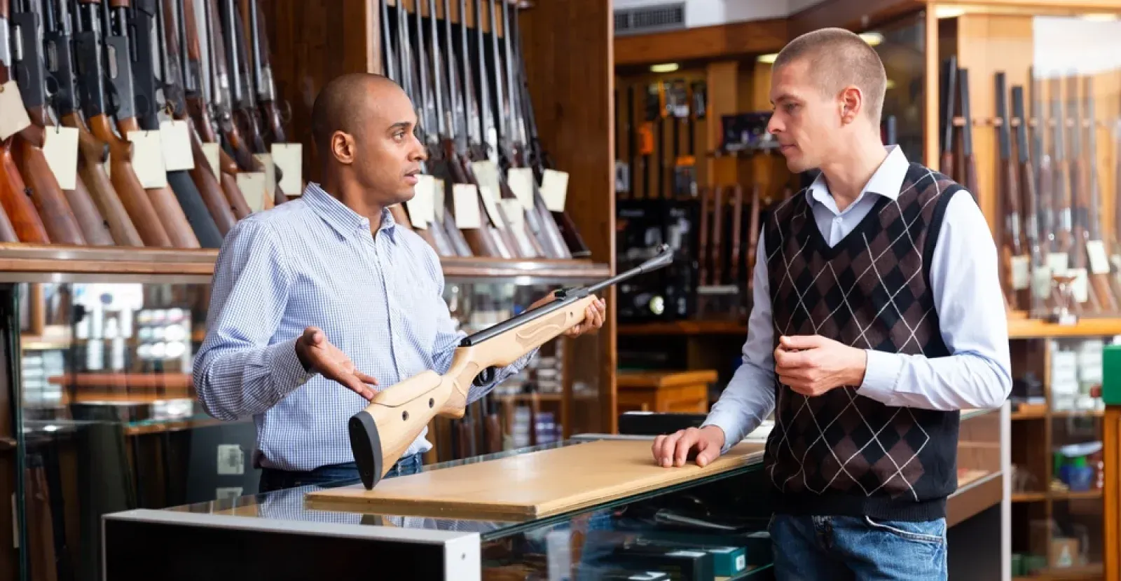 Gun shop employee talking to customer with a rifle