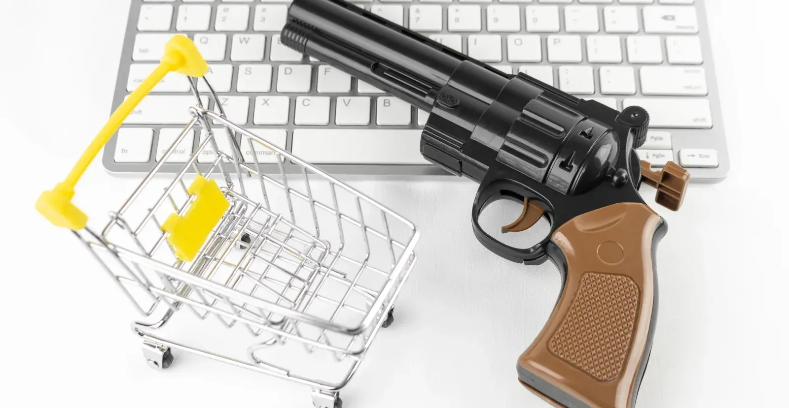 Revolver laying on keyboard next to mini shopping cart