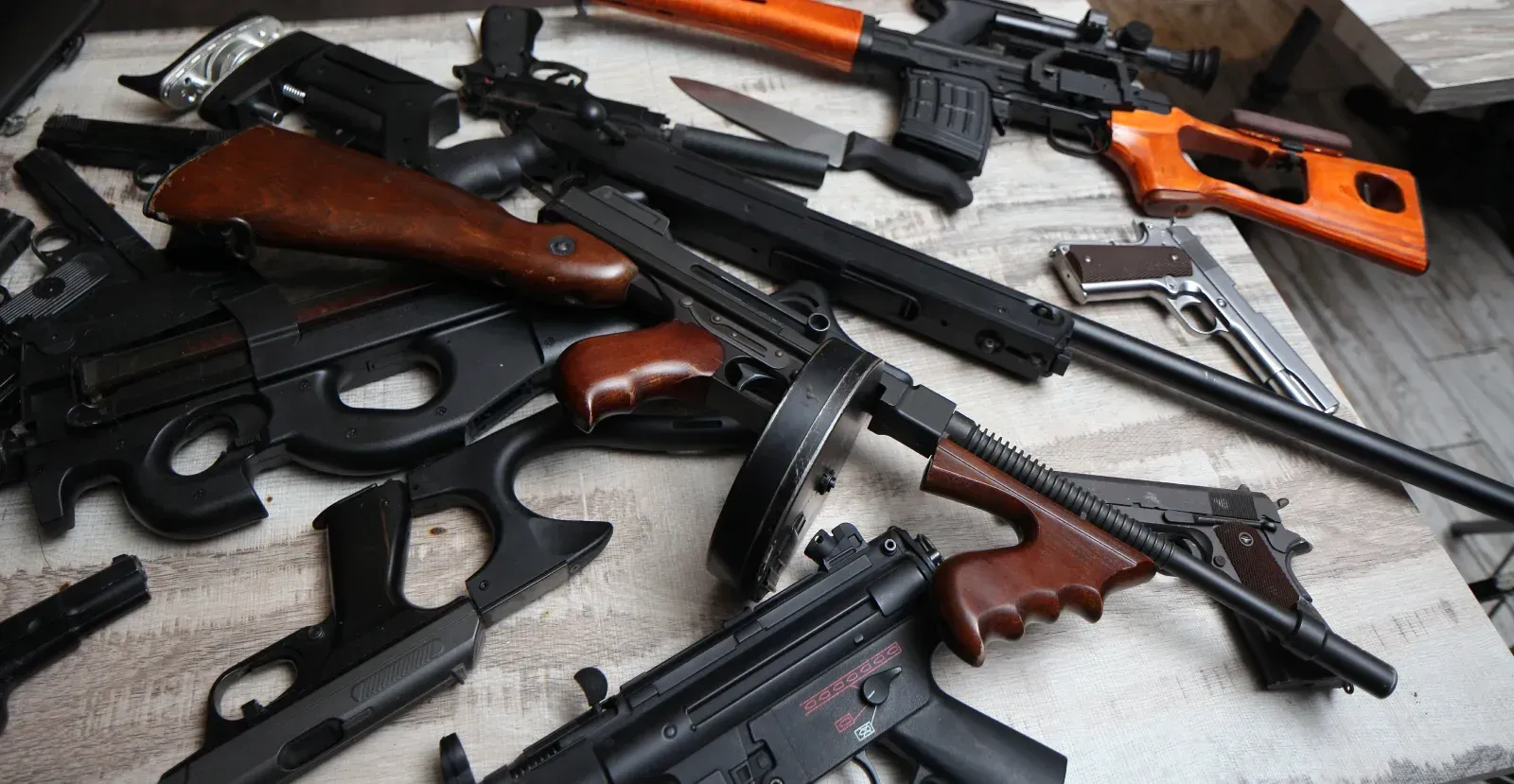 Various guns piled with a thompson submachine on top