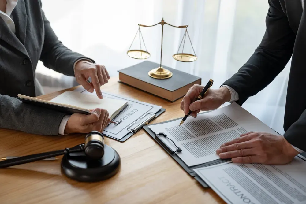 Two people looking at paperwork with scales of justice and gavel between them