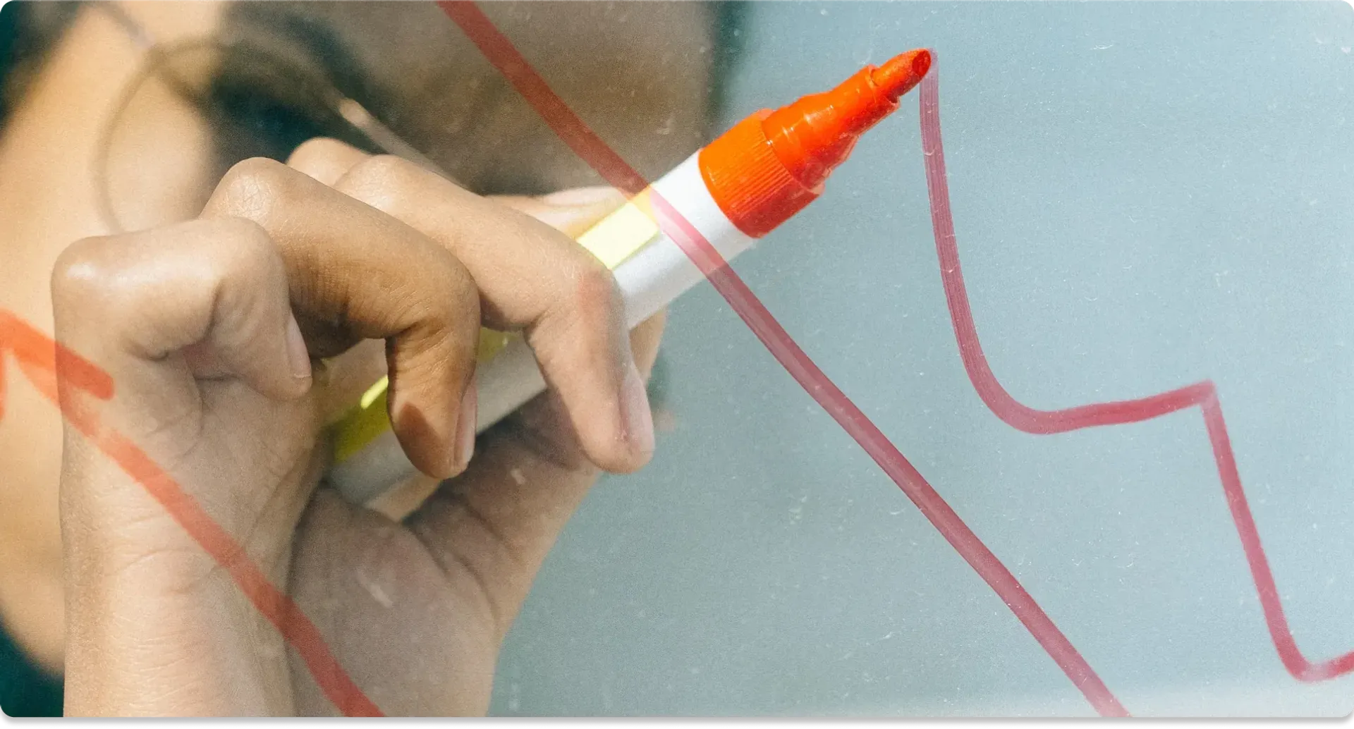 Person drawing on glass whiteboard with a red marker