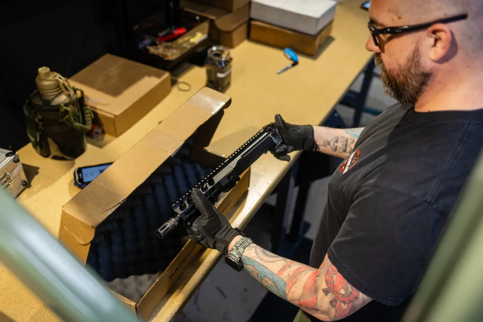 Photographing a firearm collection at the kitchen table: a collector laying out guns on a soft cloth, taking phone photos of each one with paperwork nearby.